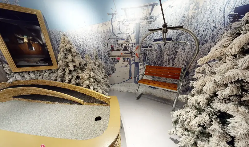 Snowy ski lift scene on the Lodge Course at Puttery Chicago with frosted trees, a chairlift seat and a winter mural backdrop.