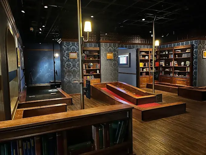 Library Course at Puttery Minneapolis with red putting lanes, dark wood bookshelves, patterned walls, and a constellation-themed section visible at the back of the course.